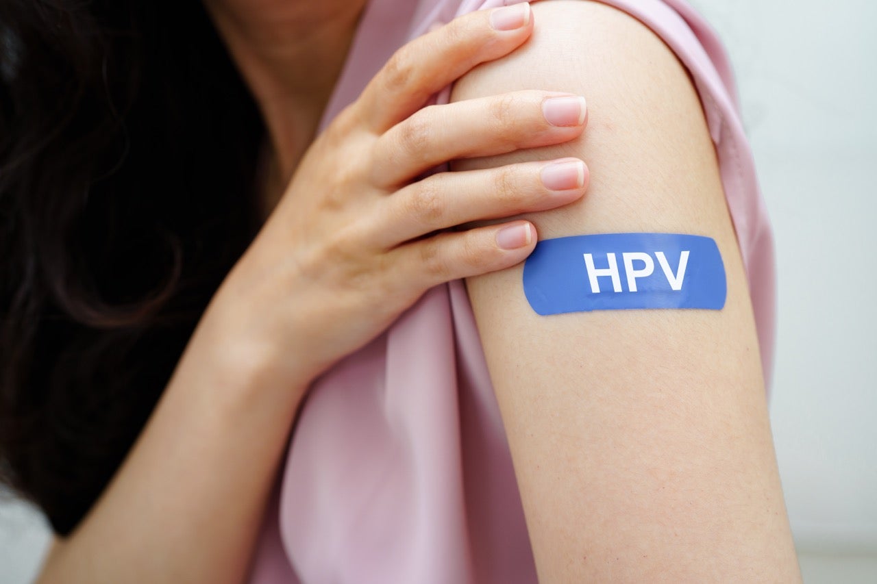 A young woman with a blue bandage on her arm who has just received a vaccination for HPV.