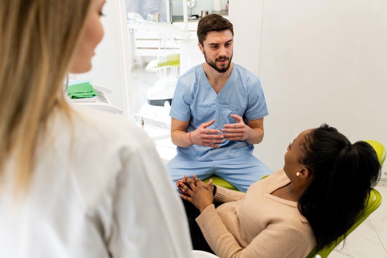 A woman talks to her dentist about excessive drooling while a hygienist listens. 