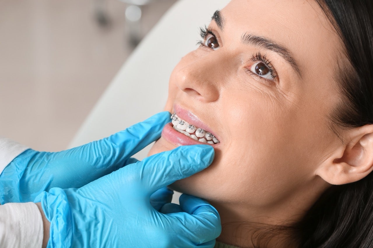 A dental hygienist moves her gloved hands against a patient’s mouth who is wearing braces.