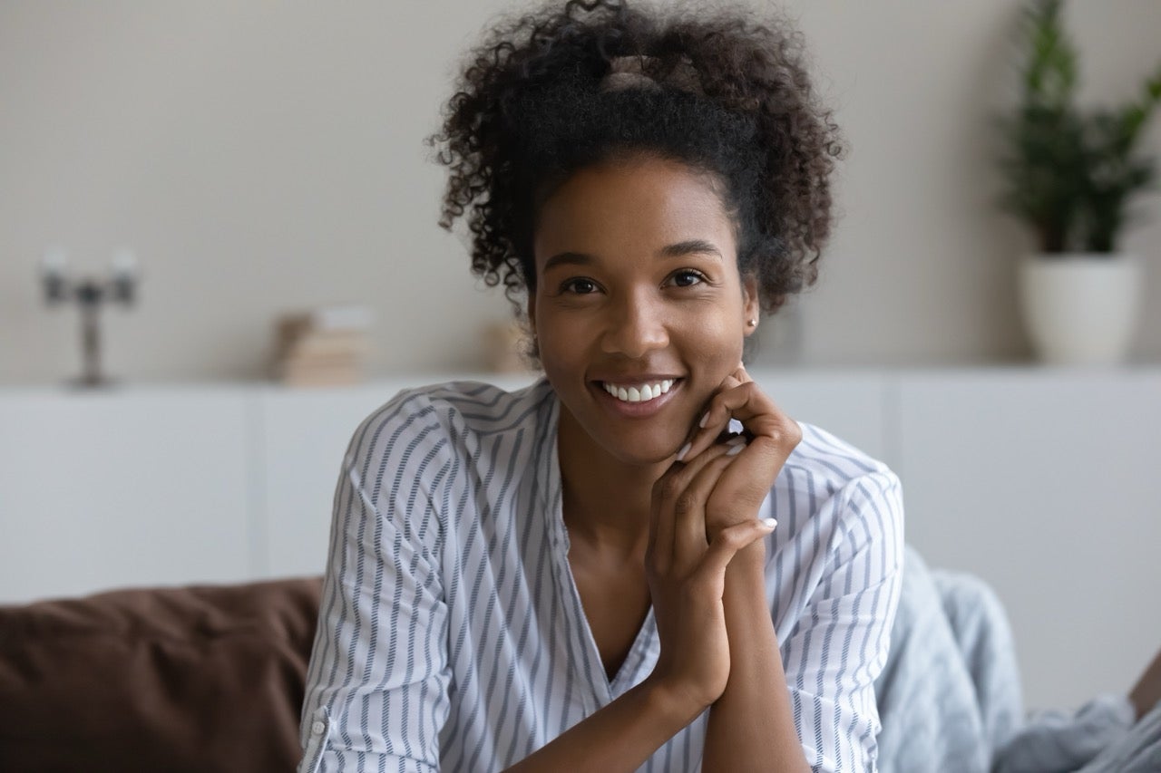 A young woman smiles as she rests her chin in her hands. 