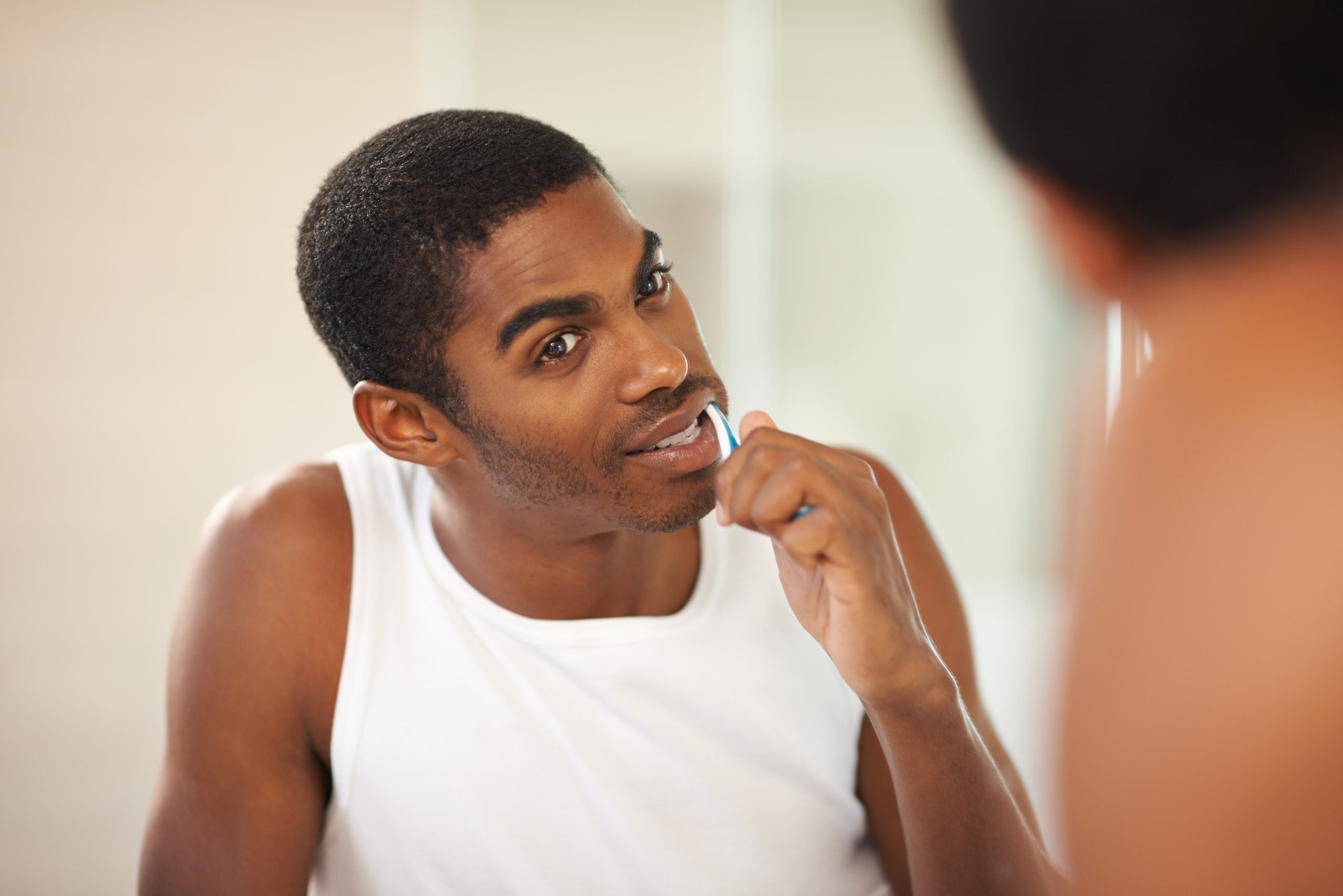 Man looks in the bathroom mirror as he brushes his straight teeth.